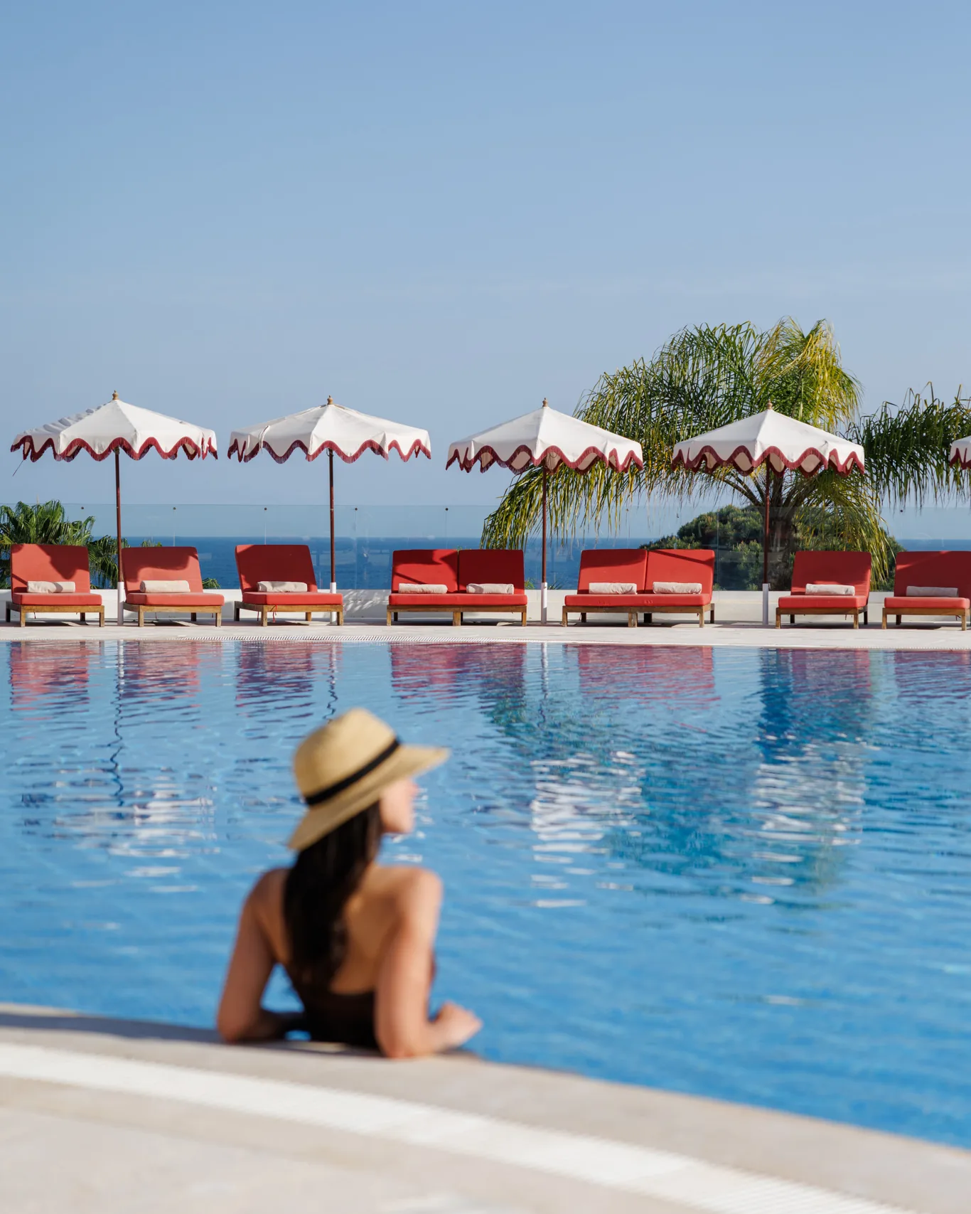 Uma hóspede na borda da piscina, chapéus de sol e o mar ao fundo