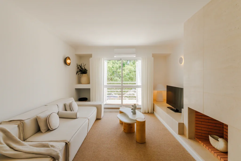 The living room of a Masana apartment, lamps lit, a cream sofa and trees beyond the window