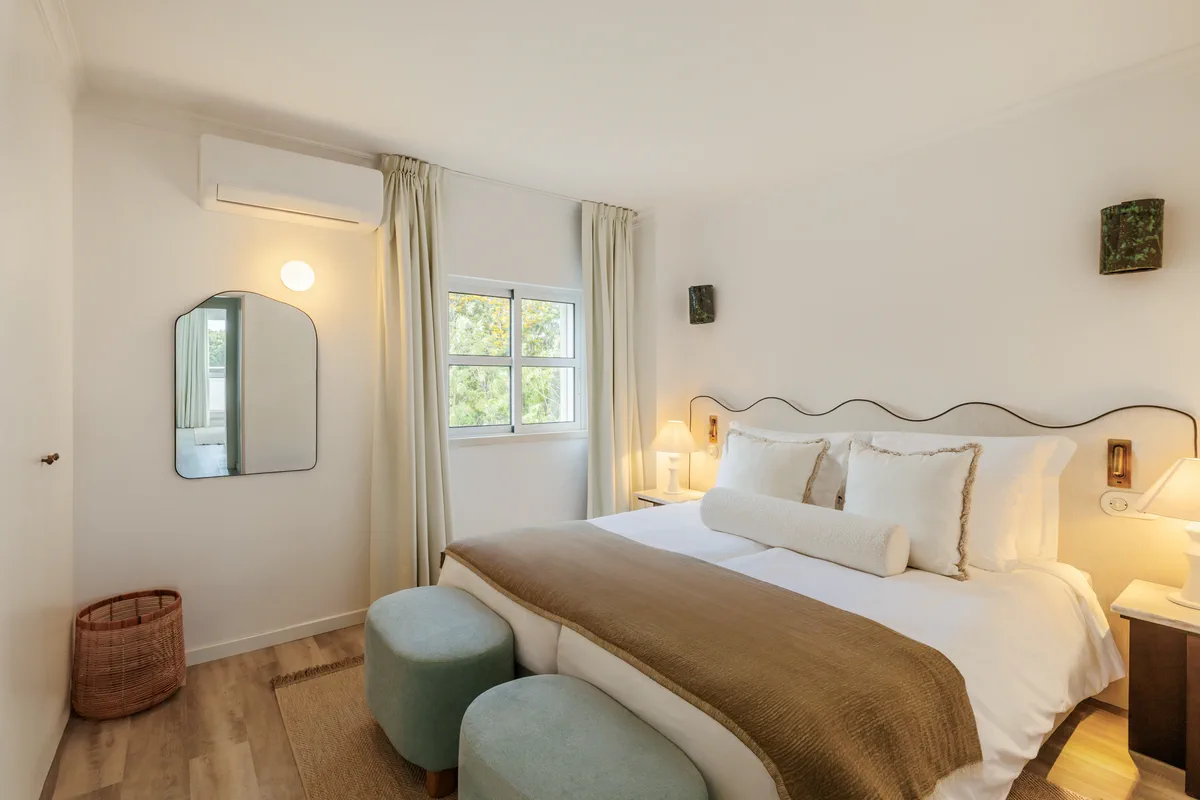 A bedroom with the lamps lit and two sage poufs