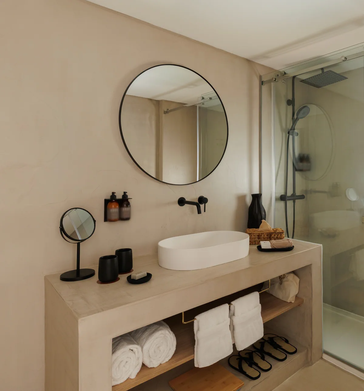 Rolled towels and slippers under a basin, a round mirror on the wall above