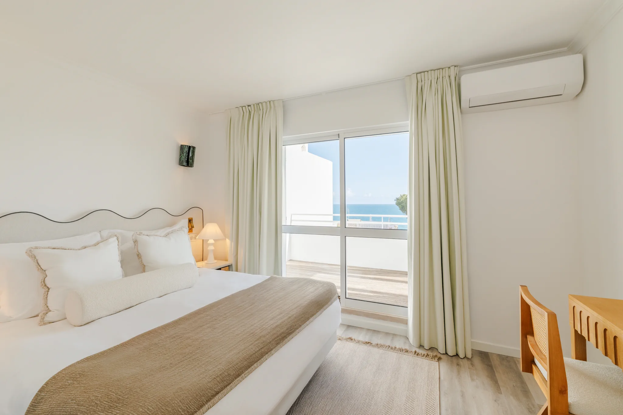 A bedroom with a wavy headboard and a window onto the sea