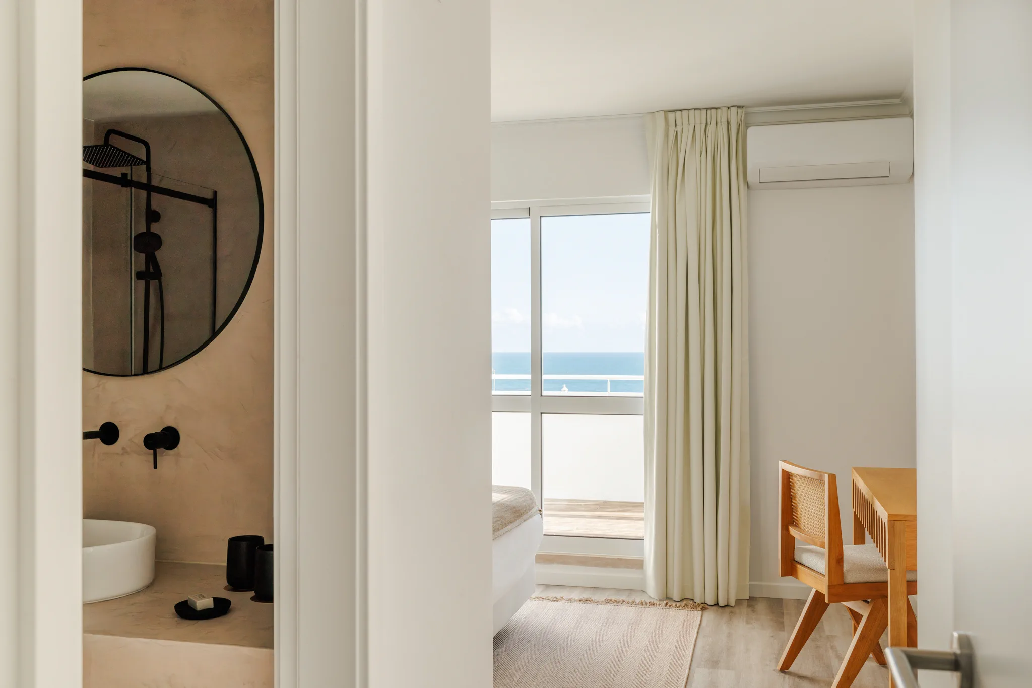 A round bathroom mirror, and through the door a bedroom with a view of the sea