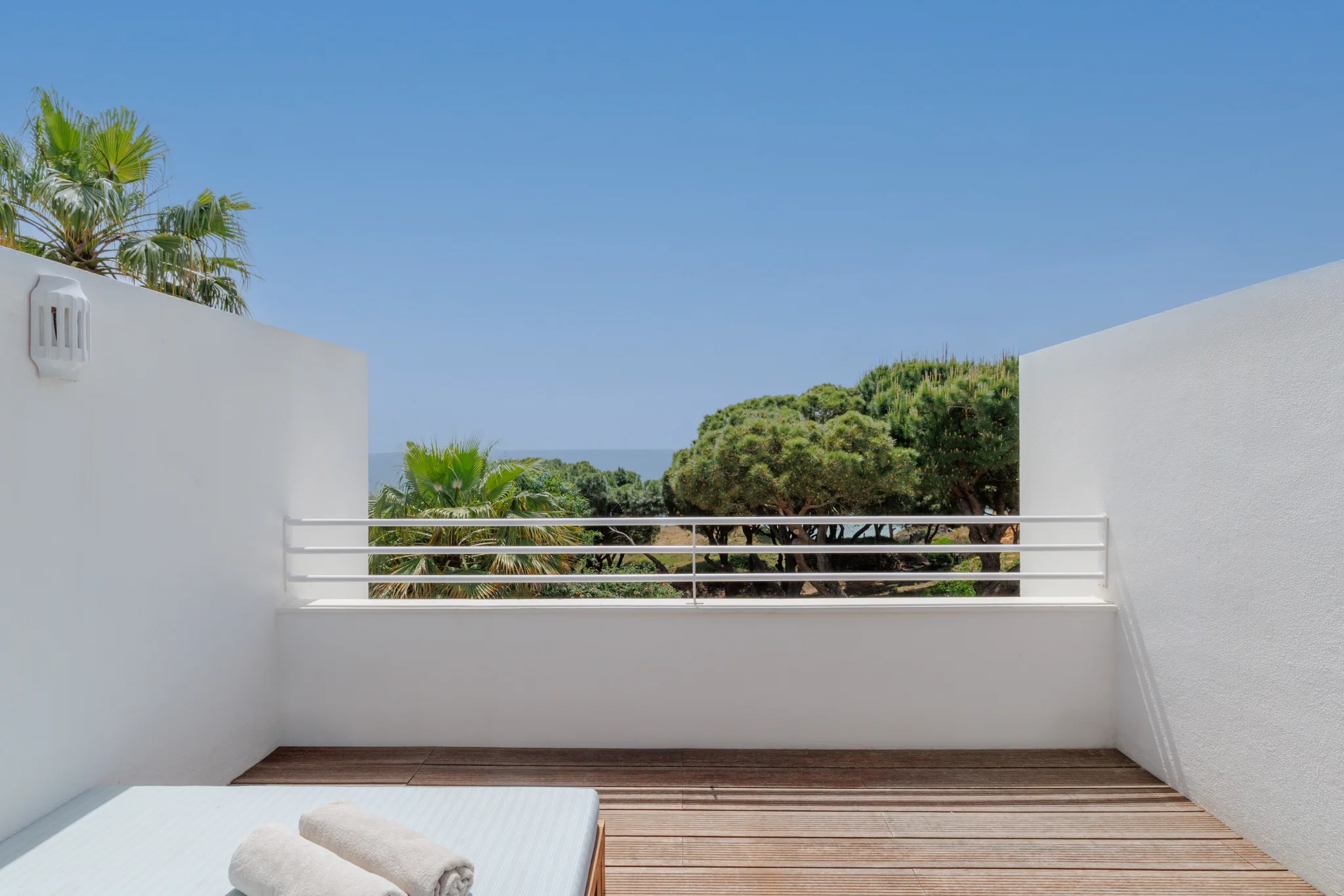 A daybed on a white terrace, stone pines and a glimpse of the sea beyond