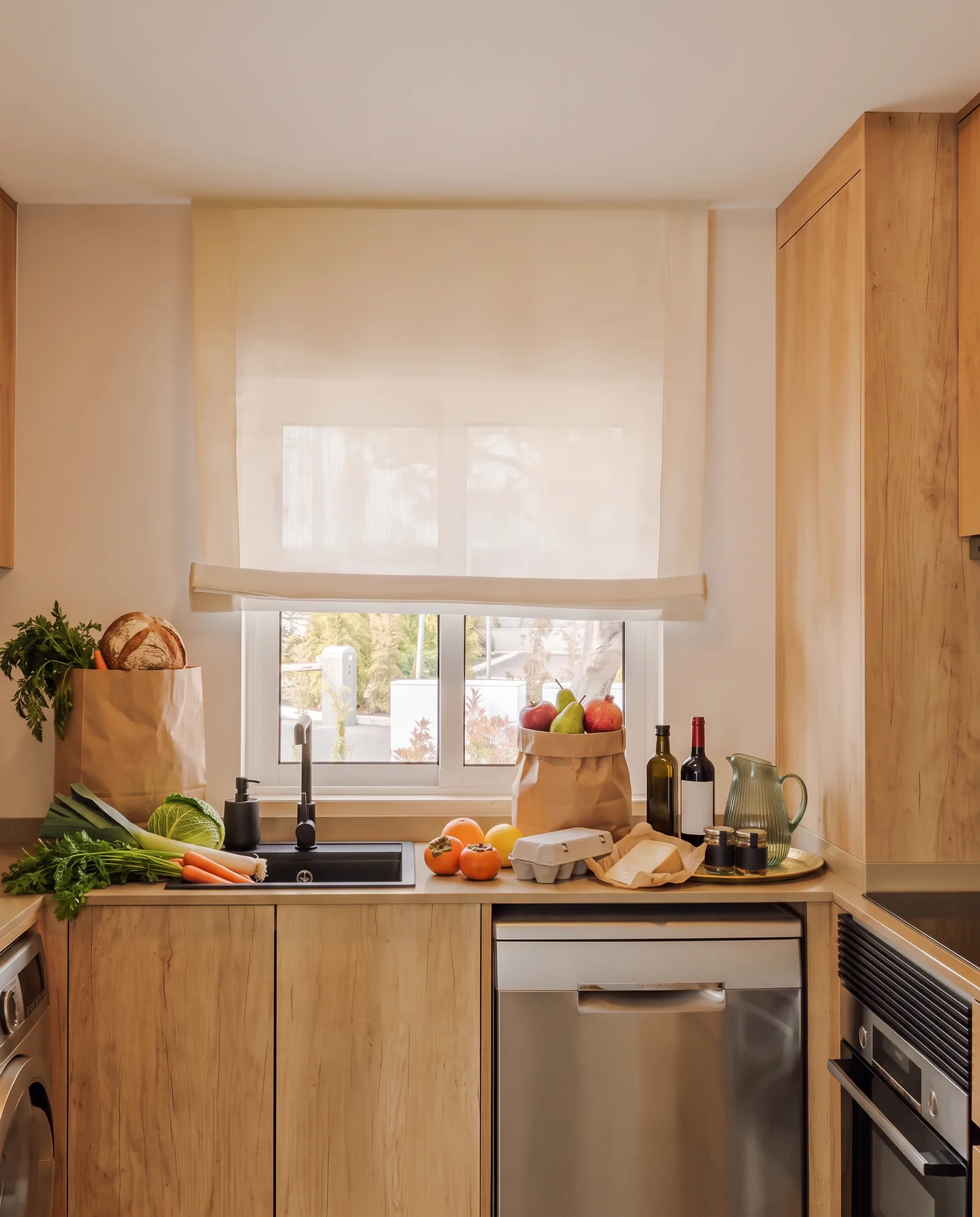 Paper grocery bags, bread, greens, pears, apples, pomegranates, persimmons, eggs, cheese, olive oil and wine on an apartment kitchen worktop